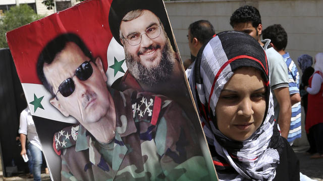 A Syrian national living in Beirut holds a picture of Syrian President Bashar Assad and Hezbollah leader Sayyed Hassan Nasrallah as she arrives to cast her vote 