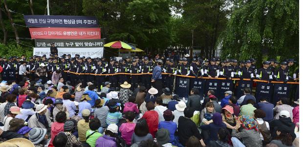 South Korean policemen stand guard in front of the main gate of the Evangelical Baptist Church premises, as church believers sit in front of the police barricade, in Anseong. 