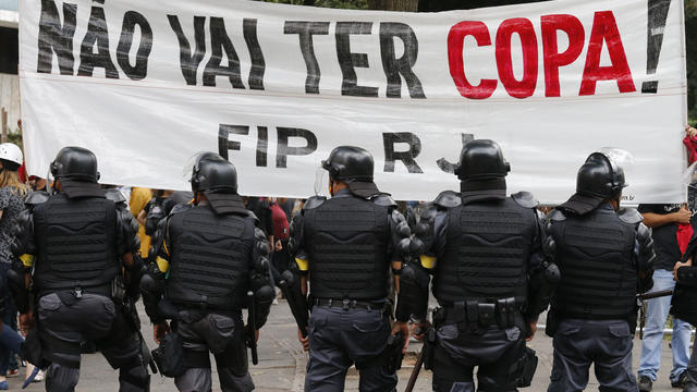 Police officers stand guard in front of a banner during a protest against the 2014 World Cup in Rio de Janeiro June 12, 2014. 