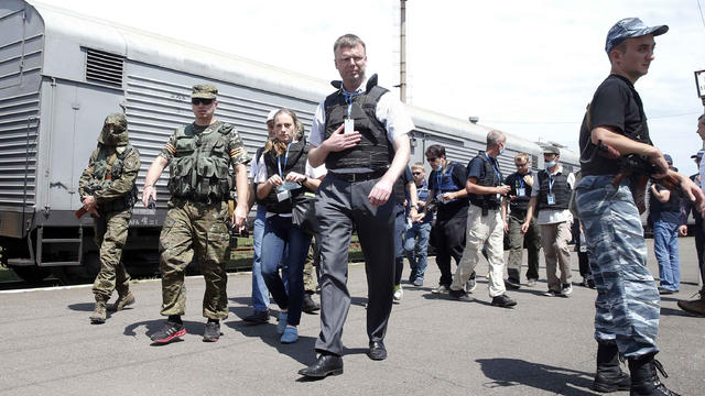 Monitors from the Organization for Security and Cooperation in Europe (OSCE), flanked by pro-Russian gunmen, walk near a train containing the bodies of passengers of Malaysia Airlines flight 17 