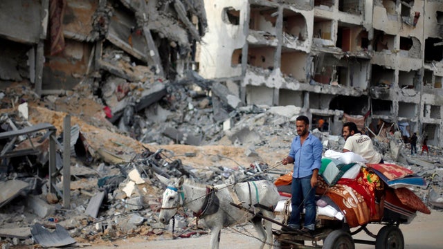 Palestinians ride a donkey cart past destroyed residential buildings as they return to Beit Lahiya town, which was hit by Israeli shelling 