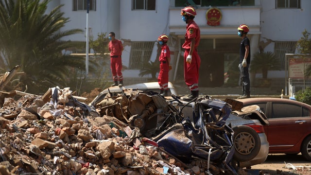 Rescue crew members watch as machinery is used to dig through the rubble of collapsed houses at Longtoushan 