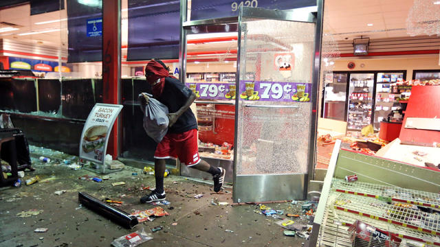 A man runs out of a a store in Ferguson, Mo., as local businesses are looted and vandalized 