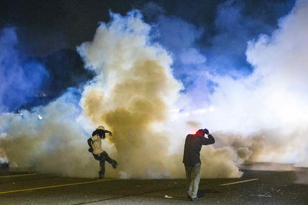 Protester kicks tear gas canister back toward police during demonstrations in Ferguson, Mo. on night of August 7, 2014 