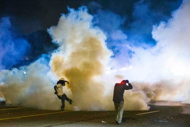 Protester kicks tear gas canister back toward police during demonstrations in Ferguson, Mo. on night of August 7, 2014