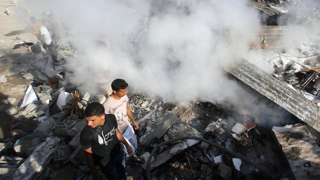 Smoke rises as Palestinians stand atop the rubble of a house, which witnesses said was destroyed in an Israeli airstrike, in Rafah in the southern Gaza Strip 