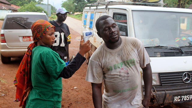 A health worker, left, uses a thermometer to screen a man at a makeshift road block run by Guinean security forces outside the town of Forecariah 