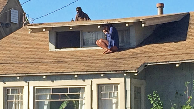 Melora Rivera, who fled her house through an attic window to escape an intruder, seen on the roof behind her, waits for help after an early-morning break in at her house in the Venice neighborhood of Los Angeles, Sept. 24, 2014. 