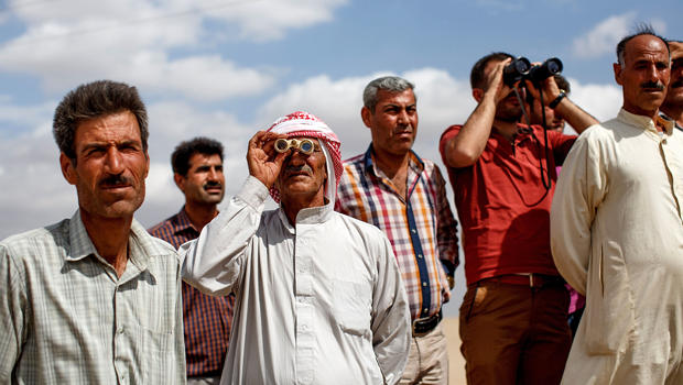 Two Kurdish men look through binoculars as Kurdish people from the region gather next to the borderfence in Suruc, Turkey, Sept. 27, 2014, to see the fighting between the Islamic State of Iraq and Syria and Kurdish Peshmergas. 
