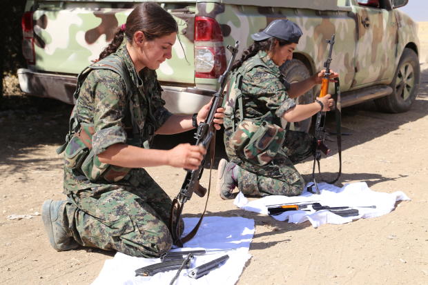 Two young female Kurdish fighters clean their weapons in a sheltered position, just a mile from ISIS militants, in the northern Syrian town of Mahmoodin 
