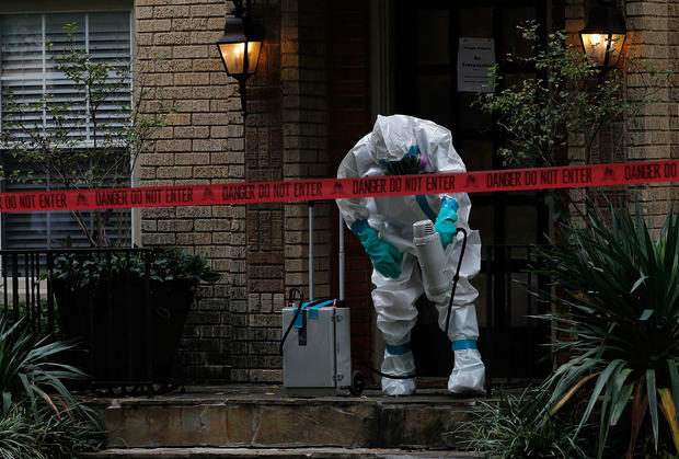 A man dressed in protective hazmat clothing treats the front porch of an apartment where a second person diagnosed with the Ebola virus resides 