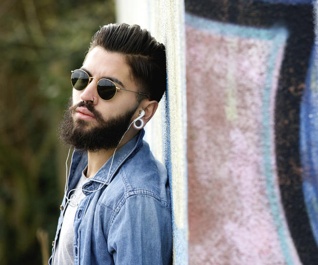 Modern young man with beard listening to music with earphones piercing guy style headphones  