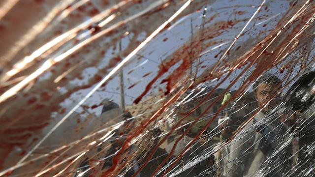 A man is seen through bloodstained and shattered glass of a vehicle damaged by a remote-controlled bomb, at the site of an incident in Kabul 