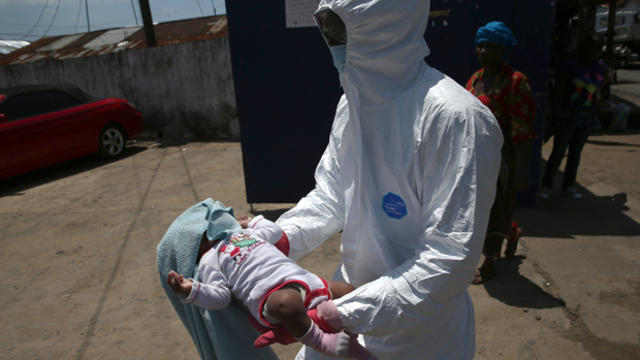 A health worker carries Benson, 2 months, to a re-opened Ebola holding center in the West Point neighborhood Oct. 17, 2014, in Monrovia, Liberia. 