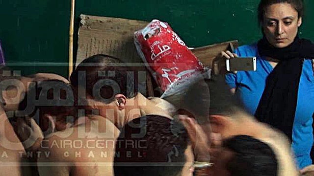 ​An image from Egyptian satellite channel Al-Qahira wa al-Nas shows journalist Mona Iraqi, (rear, right) photographing men arrested during a police raid on a public bathhouse in Cairo 