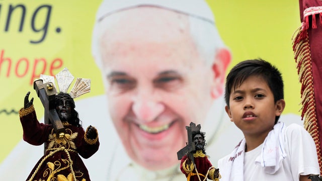A devotee walks past a banner of Pope Francis, next to replica statues of the Black Nazarene, during a procession in Manila, Jan. 7, 2015.  