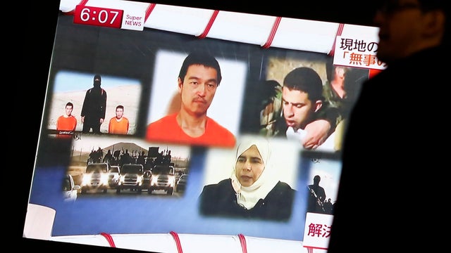 A man walks past a TV screen broadcasting a news program about ISIS hostages Muath al-Kasaesbeh (top R) and Japanese journalist Kenji Goto (top C), along a street in Tokyo 
