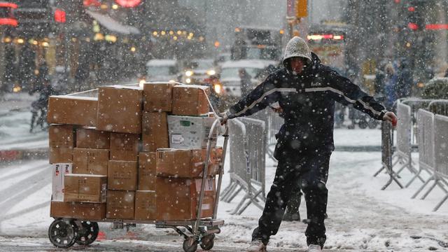 ​FedEx delivery man pulls cart loaded with packages along snowy street in Times Square in New York on February 2, 2015 