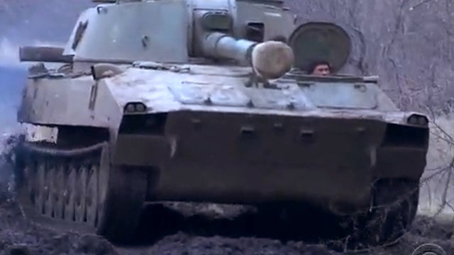 A ​Ukrainian soldier's head pokes out of a tank as he maneuvers it near the frontline in the country's east 