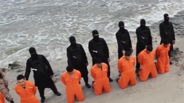 Men in orange jumpsuits purported to be Egyptian Christians held captive by ISIS kneel in front of armed men along beach said to be near Tripoli, in image from video made available on social media on Feb. 15, 2015 