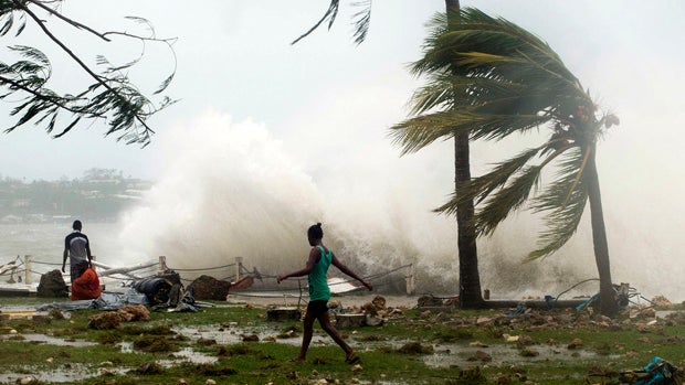 Local residents walk past debris as a wave breaks nearby in Port Vila, the capital city of the Pacific island nation of Vanuatu, March 14, 2015. 