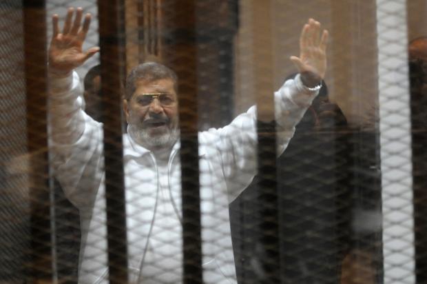 Egypt's deposed president Mohamed Morsi waves from inside the defendants cage during his trial 