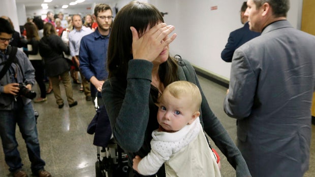 Tianna Hazard, of Oakland, California, wipes tears from her eyes as she and her daughter, Livi, 9 months, leave a committee hearing where lawmakers approved a measure requiring California schoolchildren to get vaccinated at the Capitol in Sacramento April 