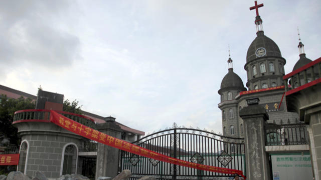 A church member of Zengshan Village Christian Church stands near rocks piled up in front of the gate to prevent government workers from moving in equipment to demolish the cross, in Zengshan village, in eastern China's Zhejiang province, July 16, 2014. Th 