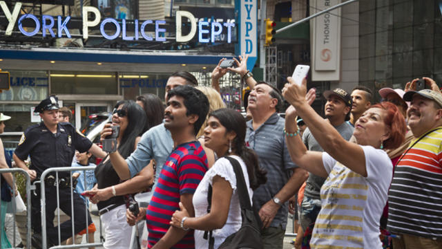 A New York police officer stands watch as visitors stage selfies for a giant monitor playback in Times Square July 3, 2015, in New York. 