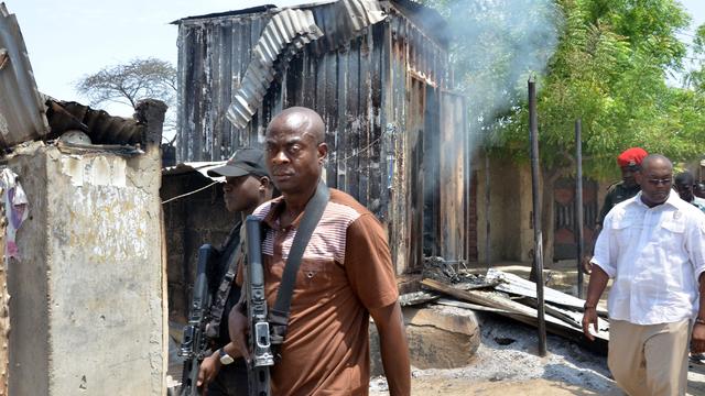 ​Security operatives walk past houses burnt by Boko Haram Islamists at Zabarmari, a fishing and farming village near Maiduguri, northeast Nigeria 