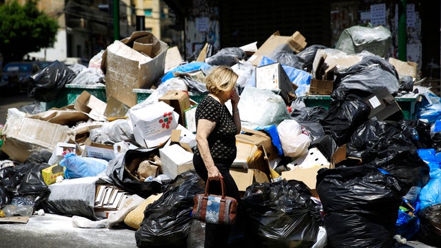 A Lebanese woman holds her nose from the smell as she passes by a pile of garbage on a street in Beirut, Lebanon 