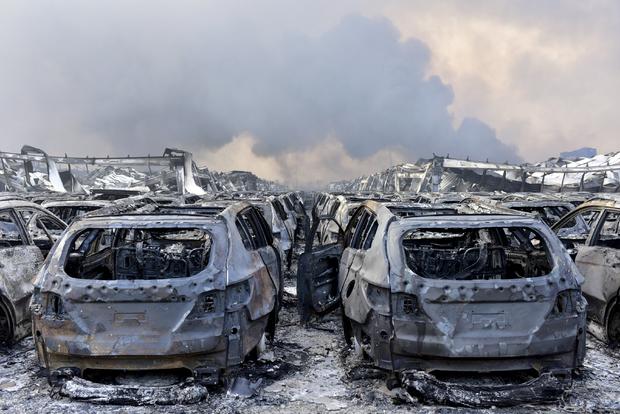 Damaged vehicles are seen as smoke rises from debris after explosions in Tianjin, China, August 13, 2015 