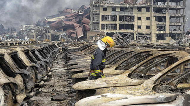 A firefighter walks among damaged vehicles as smoke rises amid shipping containers at the site of deadly explosions at Binhai new district in Tianjin, China, Aug. 14, 2015. 