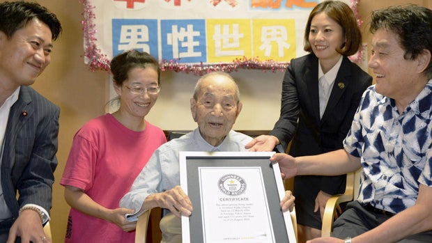 Japanese Yasutaro Koide, center, 112, receives the Guinness World Records certificate as he is formally recognized as the world's oldest man at a nursing home in Nagoya, Japan, in this photo taken by Kyodo Aug. 21, 2015. 