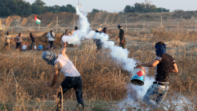 A Palestinian protester throws back a tear gas canister fired by Israeli troops during clashes near the border between Israel and the Central Gaza Strip Oct. 15, 2015. 