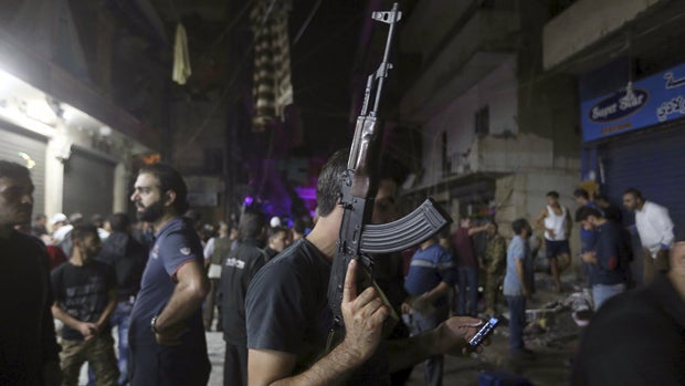 A man carrying a gun uses his mobile phone in a damaged area caused by two explosions in the southern suburbs of Beirut, Lebanon, Nov. 12, 2015. 
