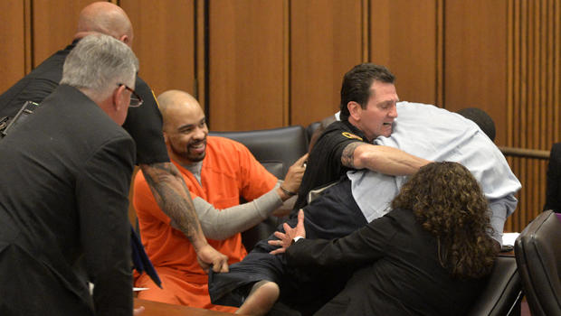 A court officer tackles the father of one of three victims of Ohio serial killer Michael Madison, left, who leaped over a table to attack the defendant in court just minutes after the judge pronounced a death sentence in Cuyahoga County Common Pleas Court 