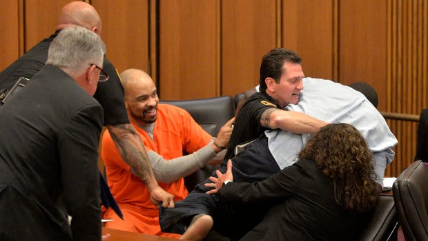 A court officer tackles the father of one of three victims of Ohio serial killer Michael Madison, left, who leaped over a table to attack the defendant in court just minutes after the judge pronounced a death sentence in Cuyahoga County Common Pleas Court 