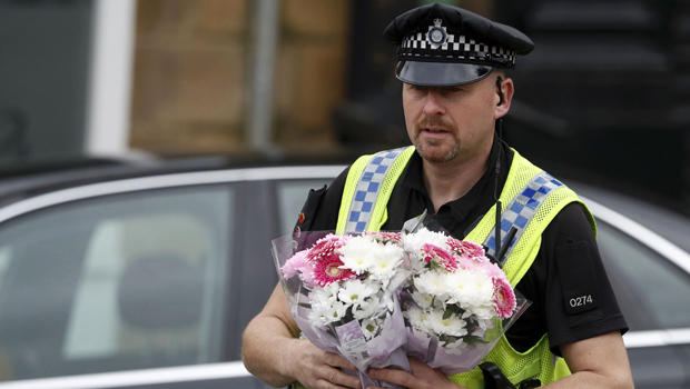 A police officer carries bunches of flowers at the scene of the murder of Labour MP Jo Cox in Birstall near Leeds, England, June 16, 2016. 