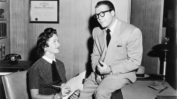 George Reeves as 'Clark Kent' sits on desk beside Noel Neill, as 'Lois Lane' 