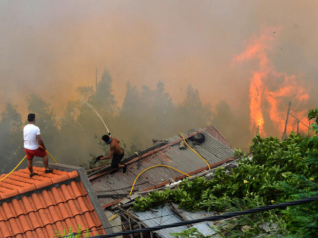 Men spray water on the roofs of houses to protect them from an approaching fire in Portugal's Maderia islands 