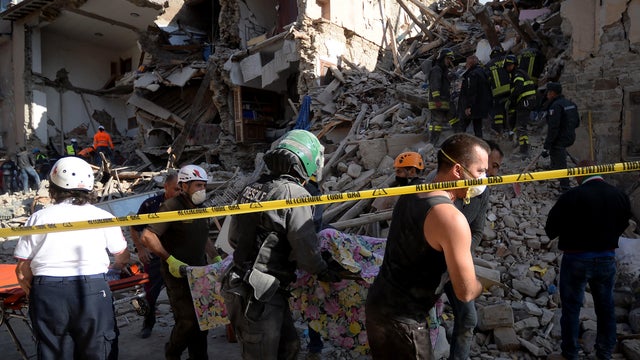 Rescuers carry the body of a victim next to the rubble of buildings in Amatrice 