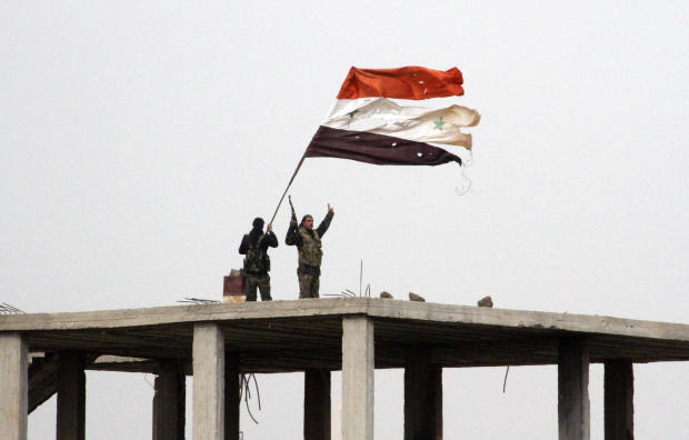 Syrian government forces wave the Syrian flag while standing on top of a building in Deir al-Adas, Syria, on Feb. 11, 2015, after President Bashar Assad’s army, backed by Hezbollah and Iranian officers, pushed rebels out of the area. 