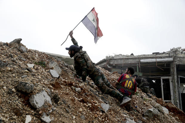 A Syrian army soldier places a Syrian national flag during a battle with rebel fighters at the Ramouseh front line, east of Aleppo, Syria, Dec. 5, 2016. 