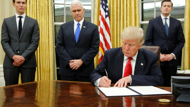President Trump, flanked by, from left to right, senior adviser Jared Kushner, Vice President Mike Pence and Staff Secretary Rob Porter, signs his first executive orders in the Oval Office at the White House in Washington Jan. 20, 2017. 