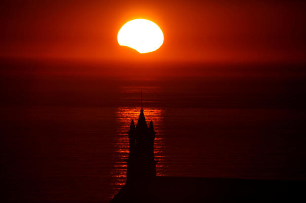 The Saint-They Chapel is seen in silhouette at sunset during a partial solar eclipse as the moon passes in front of the sun seen at the Pointe du Van 