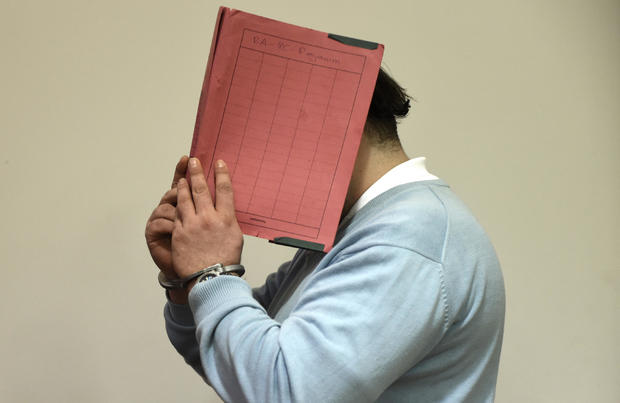 Former nurse Niels H. masks his face with a folder on his arrival in the courtroom in Oldenburg 