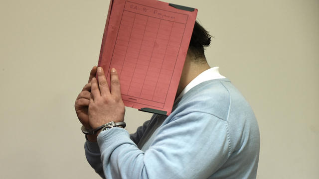 Former nurse Niels H. masks his face with a folder on his arrival in the courtroom in Oldenburg 