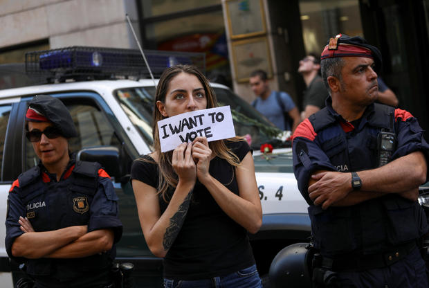 A protestor holds up a sign in front of a Catalan police outside the Catalan region's foreign affairs ministry building during a raid by Spanish police on government offices, in Barcelona 