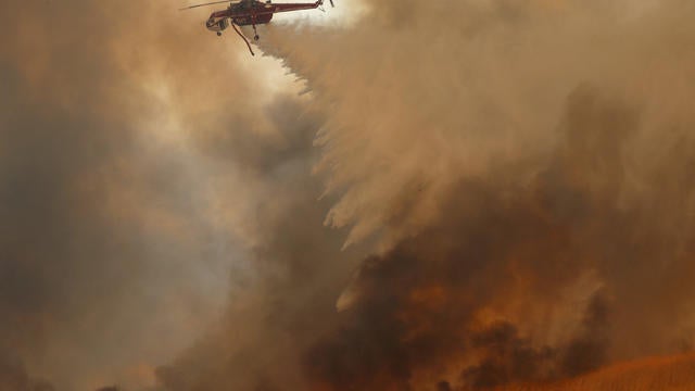 A helicopter drops water on a wind driven wildfire in Orange, California 